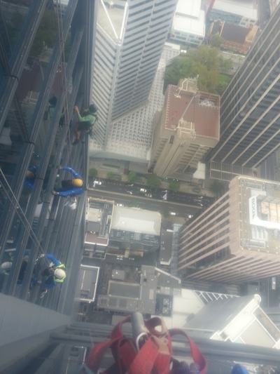 Looking down the face of a skyscraper, with rope access technicians working on the façade far above the street